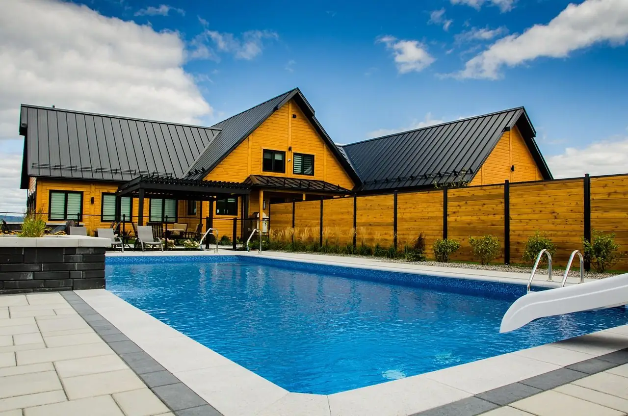 Finished rectangular in-ground pool with a white coping edge beside a modern house