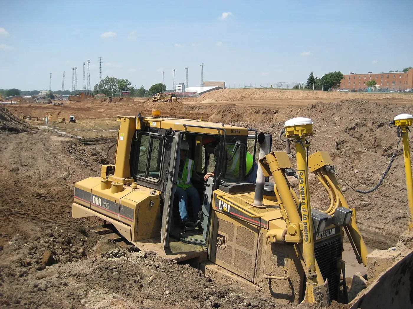 Yellow bulldozer with GPS receivers on masts working a graded dirt site