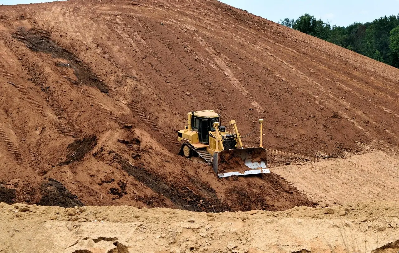 Small yellow bulldozer pushing dirt up the face of a large brown earth slope