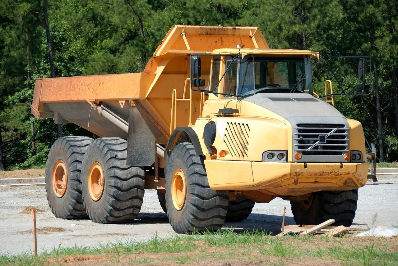 Yellow articulated dump truck parked on a cleared dirt site with trees behind