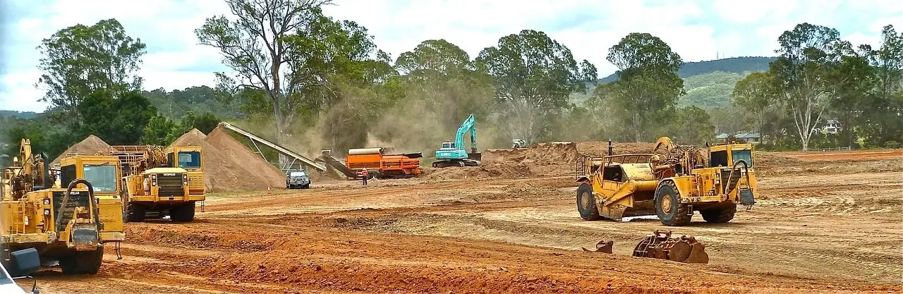 Wide view of a large dirt construction site with dozers and scrapers moving earth under a blue sky