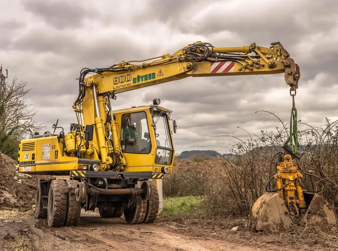 Yellow wheeled excavator with a grapple attachment working at a rural site